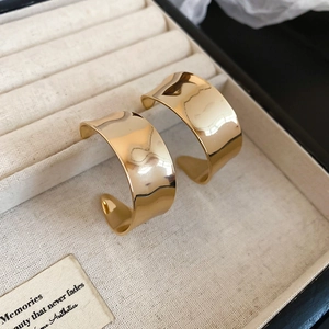 Nahaufnahme von polierten goldenen breiten C-Ohrringen in einer beigen Samt-Schmuckschatulle