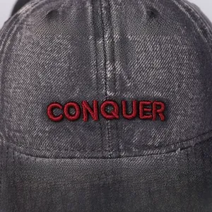 Macro shot of red 3D CONQUER embroidery on vintage washed denim baseball cap