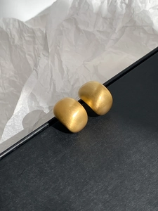 Detailed macro shot of matte gold semi-cylindrical earrings with brushed metal texture