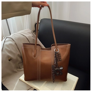 Detail of glossy brown tote bag with contrast stitching and cat charm for work