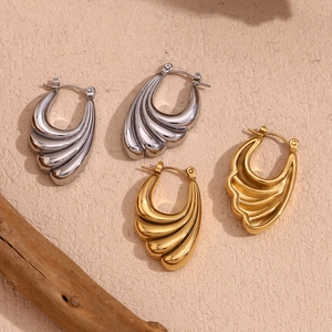 Detailed view of wave-shaped 18K gold and silver earrings on a minimalist wood base