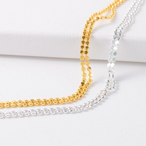 Macro detail of gold and silver double-layered disc chain necklaces on white background