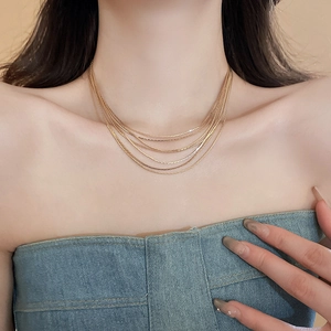 Nahaufnahme mehrlagiger vergoldeter Halsketten an einem Model im minimalistischen Stil
