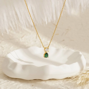 Close-up of 18K gold necklace with white zircon and emerald green drop stone