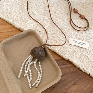 Detail of a Neo-Chinese style necklace with fruit pit pendant and pearl tassels on a rustic mat