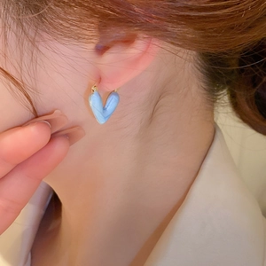 Détail de boucle d'oreille cœur bleu clair marbré avec placage en or sur l'oreille