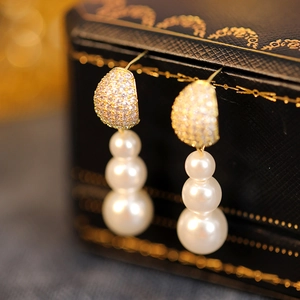 Macro detail of elegant three-tier pearl drop earrings with sparkling gold diamond-set base