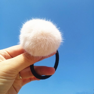 Close-up of a fluffy cream faux mink fur pom-pom hair tie against a bright blue sky