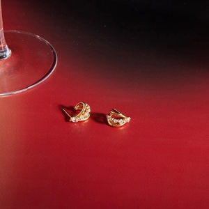 Detailed view of gold C-shaped earrings with cubic zirconia on a dark elegant background