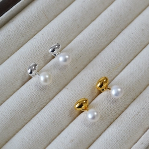 Detail of gold and silver brass earrings with freshwater pearls on a grey display tray