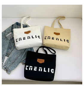 Flat lay of canvas tote bags in white, beige, and black with brand print and leather label