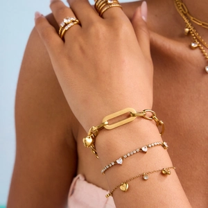 Close-up of gold heart charm bracelet and rings set with sparkling white zircon accents