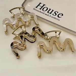 Three wavy acetate hair claws in marble, tortoiseshell, and cream with gold alloy base