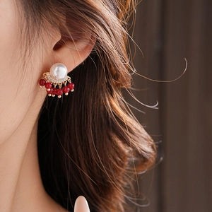 Close-up of gold fringe earrings with white pearls and red beads worn by a model