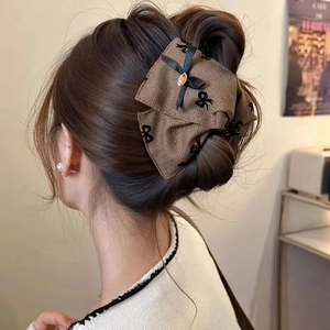 Brown fabric bow hair claw clip with black embroidery and gold pendant on model's bun