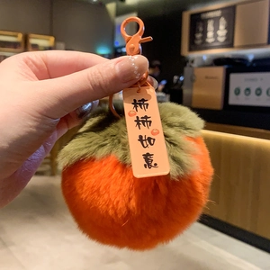 Detailed close-up of a plush persimmon charm with green leaves and a metal keychain