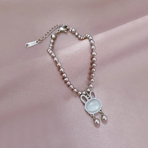 Detail shot of a silver bunny pendant bracelet with white cat-eye stone on silk fabric