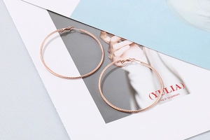 Close-up of rose gold hoop earrings with twisted rope texture on a minimalist background