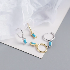 Detailed view of minimalist gold and silver hoop earrings with emerald green stone pendants