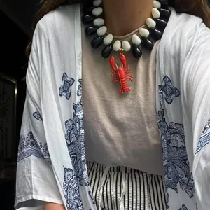 Close-up of a bold red lobster pendant necklace with black and white resin beads on a model
