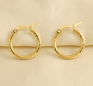 Close-up of golden stainless steel hoop earrings with twisted texture on silk cloth