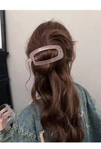 Gros plan d'une pince à cheveux ovale rose mat portée sur un chignon de style minimaliste