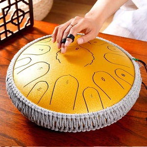 Close-up of hand playing yellow steel tongue drum with braided edge on wooden table