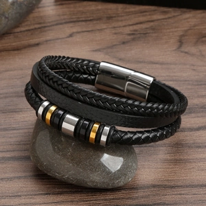 Mehrlagiges schwarzes Lederarmband mit Gold- und Silberringen auf einem grauen Stein
