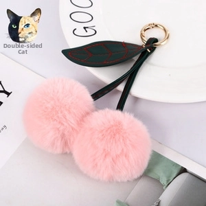 Close-up of pink faux fur cherry keychain with green leather leaves and gold metal ring