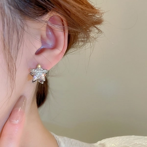Close-up of a silver star-shaped earring with zircon studs worn on a model's ear