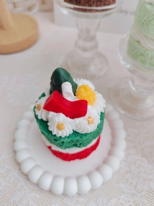 Close-up of a double-layer Christmas cake candle with a mini tree and festive decorations