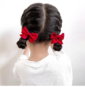 Gros plan de barrettes à nœud en satin rouge sur cheveux tressés de fille en blanc
