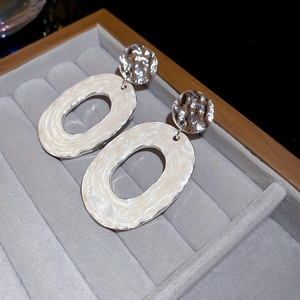 Macro shot of silver textured metal disc and oval pearl white enamel wavy pendant earrings