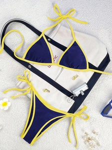 Detailed flat lay of navy and yellow contrast bikini with beach accessories on white surface