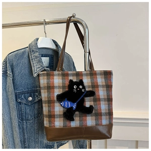 Detail of checkered tote bag with 3D black cat plush toy and brown leather handles