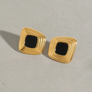 Detail view of square titanium steel earrings with a gold frame and black resin inlay