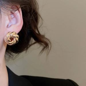 Close-up of a gold knot stud earring with a minimalist multi-strand twisted design