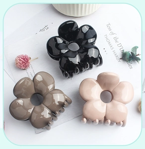 Detailed top view of three glossy floral hair claws in black, grey, and beige resin