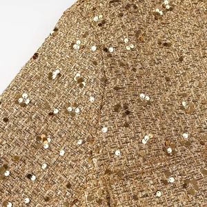 Dettaglio macro del tessuto tweed a paillettes dorate con trame metalliche intrecciate