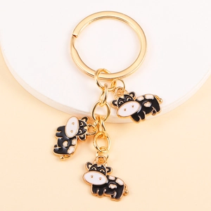 Macro shot of three cute black and white cartoon cow charms on a golden metal keychain
