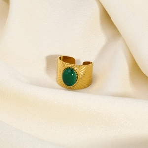 Macro di un anello in acciaio dorato con pietra verde e motivo a raggi di sole
