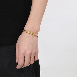 Close-up of a gold twisted cable cuff bracelet worn on wrist with metallic texture