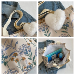 Detailweergave van beige draagtas met blauw bloemenborduurwerk en hartvormige hanger