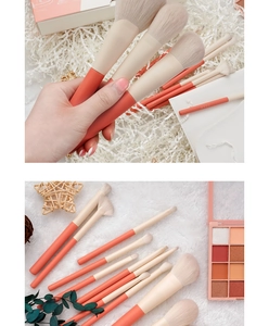 Close-up of 12pcs coral makeup brush set with soft beige bristles on white textured fabric