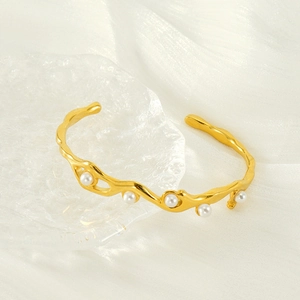 Dettaglio di un bracciale a onde placcato oro 18k con cinque perle su un piatto di vetro