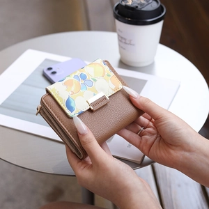 Close-up of model holding floral print PU leather wallet with gold buckle in a cafe setting