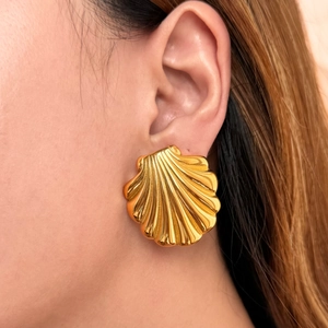 Close-up of a large gold shell earring on a model showing vintage metallic texture