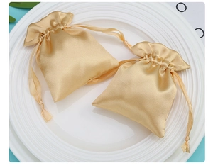 Macro shot of two golden satin drawstring gift bags with silk texture on a white plate