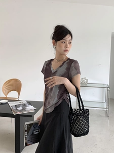 Close-up of a black hand-woven bucket bag paired with a gray-purple tie-dye V-neck T-shirt