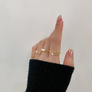 Detail of layered gold ring set with pearls and zircons on hand with black knit cuff